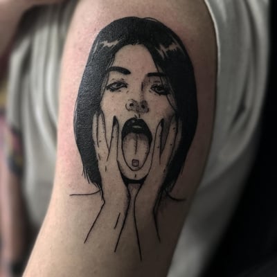 A bold blackwork tattoo of a woman's face with her tongue out on the upper arm — by Maddie Ramirez, los angeles
