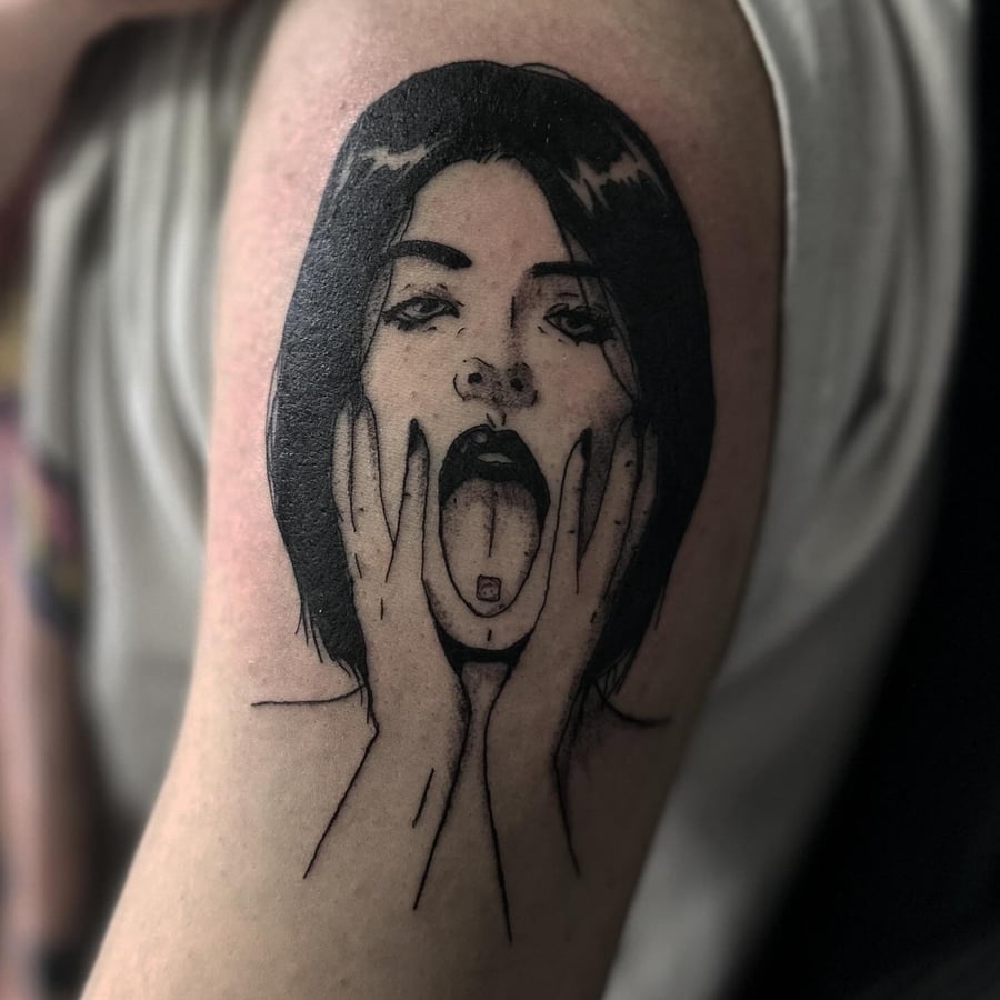 A bold blackwork tattoo of a woman's face with her tongue out on the upper arm — by Maddie Ramirez, los angeles