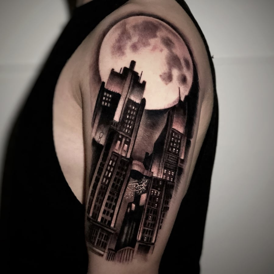 A black and grey realism tattoo of a cityscape under a full moon on the upper arm, featuring detailed buildings and soft shading — by Travis Ross, los angeles