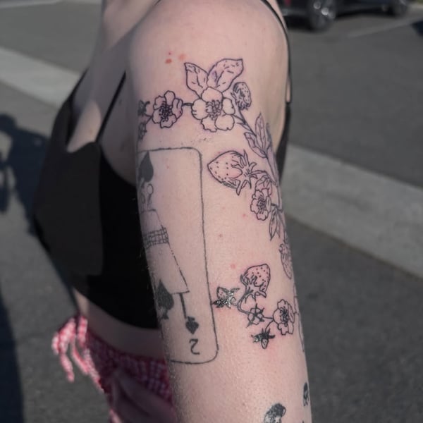 A minimalist black and grey tattoo of a playing card with floral elements on the upper arm, featuring delicate linework — by Hannah , fountain valley, ca