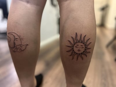 A black and grey fine line tattoo of the sun and moon on the calf — by Maddie Ramirez, los angeles