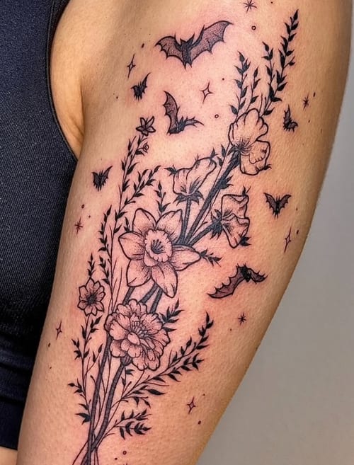 A fine line blackwork tattoo on the upper arm featuring flowers and bats with delicate details and shading — by NJ TATTOOZ, los angeles