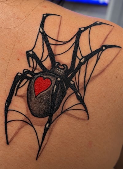 A bold black spider tattoo with a red heart on its back, placed on the shoulder — by HEAVY INK, los angeles