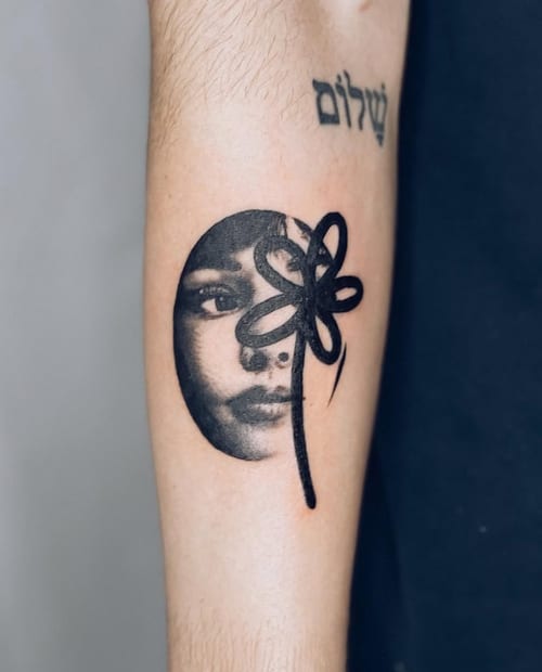 A black and grey abstract portrait of a woman's face on the forearm, featuring bold blackwork lines and shading — by Level tattoo, los angeles