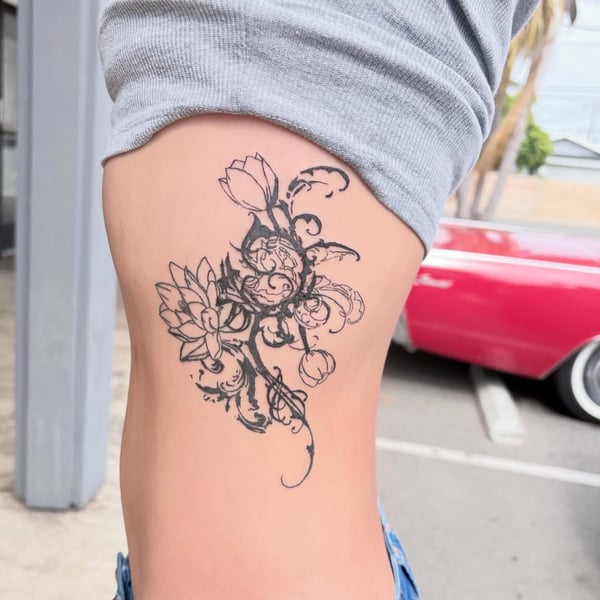 A delicate black and grey floral design tattoo on the hip, featuring intricate flower patterns in a blackwork style — by Hannah , fountain valley, ca