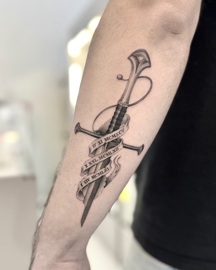A black and grey tattoo of a realistic sword with Roman numerals on the forearm, featuring detailed shading and linework — by otaybeatdown, los angeles