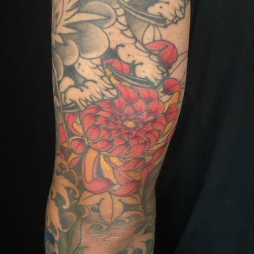 A bold Japanese style flower tattoo on the arm with vibrant red and yellow colors — by Sandra Price, los angeles