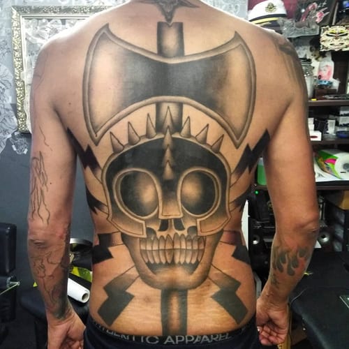 A bold black and grey tattoo of a skull with an axe on the full back, featuring graphic elements and strong shading — by Samuel Connelly, los angeles