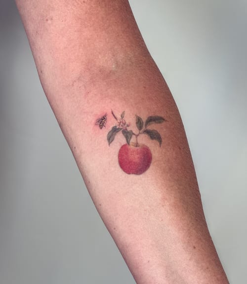 A delicate color tattoo of an apple with a bee on the forearm, featuring fine line details and realistic shading — by Melanie Benoit, los angeles