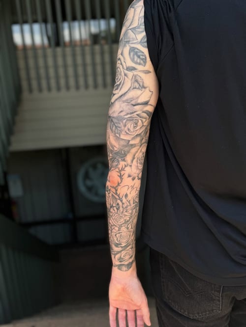 A detailed black and grey rose bouquet tattoo on the arm, featuring realistic shading and intricate floral designs — by Sandra Price, los angeles