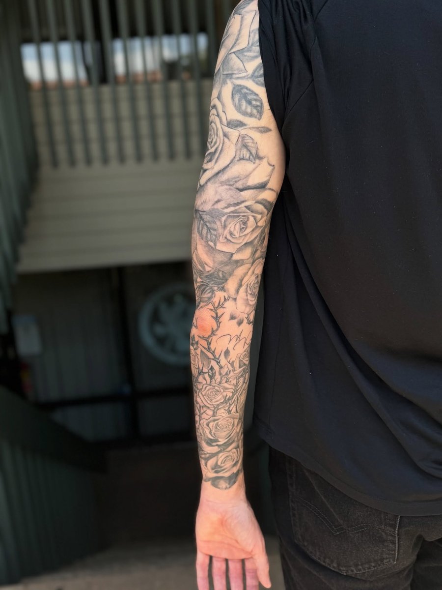 A detailed black and grey rose bouquet tattoo on the arm, featuring realistic shading and intricate floral designs — by Sandra Price, los angeles