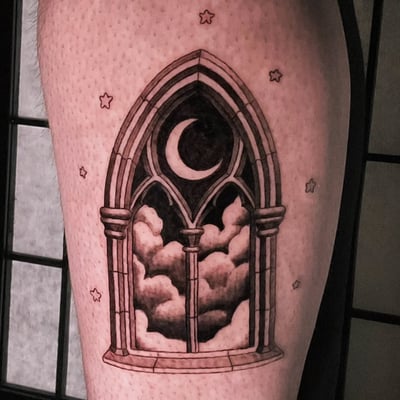 A black and grey tattoo of a gothic window with a crescent moon and clouds on the thigh, featuring ornate architectural details — by Miguel ANGELO, los angeles