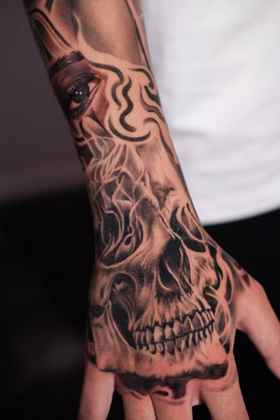 A black and grey realism tattoo on the hand featuring a detailed skull and eye with intricate shading — by Johnny Ayala, los angeles