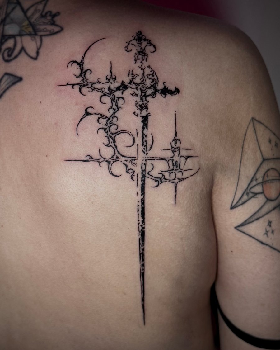 A black and grey ornamental sword tattoo on the back with intricate detailing and sharp lines — by emily, los angeles
