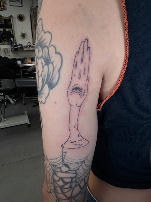 A minimalist linework tattoo of a hand with an eye in the palm on the upper arm, using black ink — by Hannah , los angeles