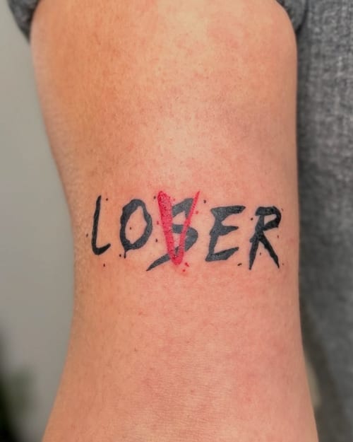 A minimalist lettering tattoo on the arm with the word 'LOSER' altered to 'LOVER' using red ink — by NJ TATTOOZ, los angeles