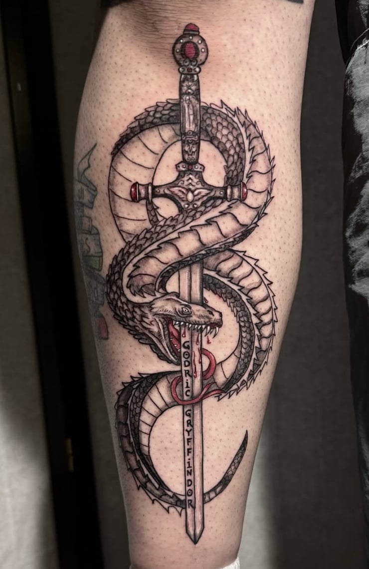 A black and grey Neo-Traditional tattoo of a snake coiled around a sword on the leg, featuring intricate linework and shading — by Shelby Bianco, los angeles