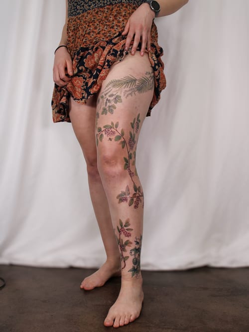 A colorful floral vine tattoo extending from the thigh to the lower leg, featuring delicate flowers and leaves in a fine line style — by Melanie Benoit, los angeles