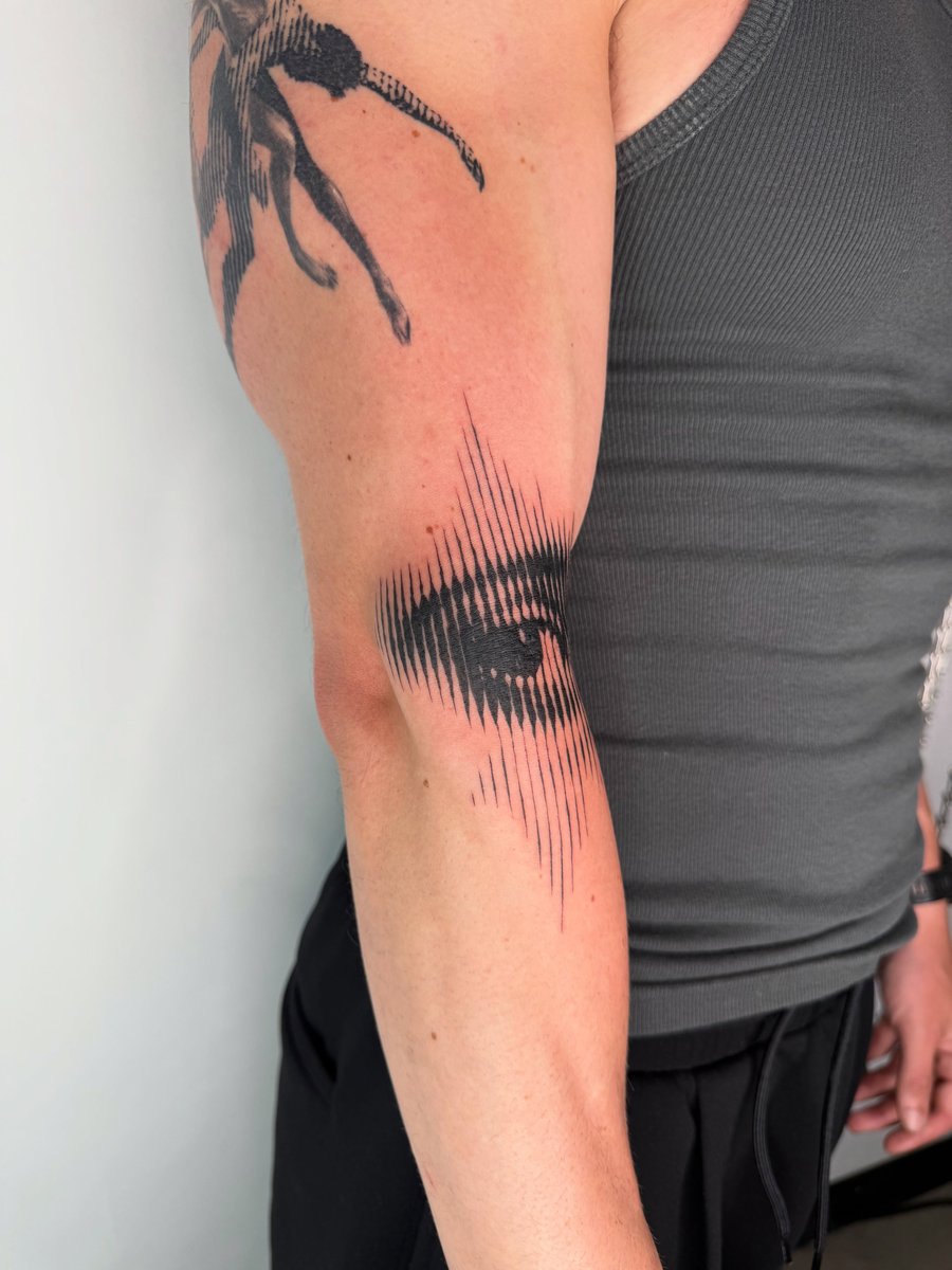 A graphic blackwork tattoo of an eye with a line pattern on the upper arm, featuring bold black ink — by Level tattoo, los angeles