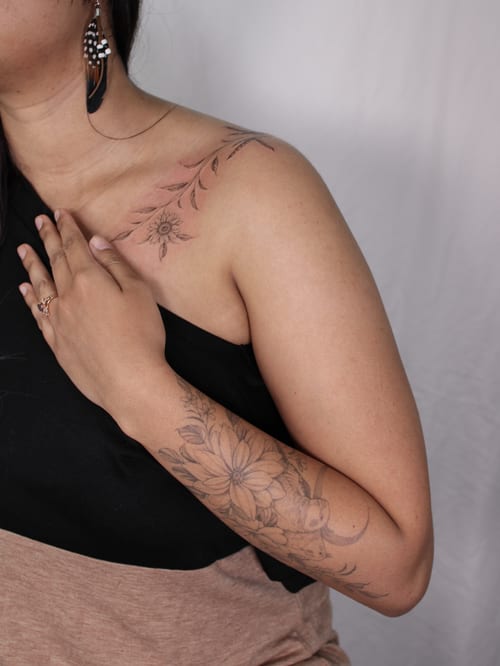 A delicate black and grey floral tattoo on the shoulder and arm, featuring fine line work and elegant flower designs — by Melanie Benoit, los angeles