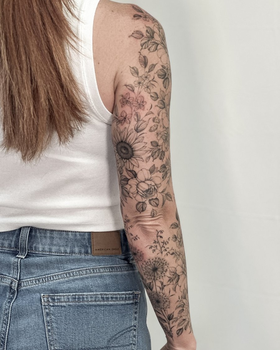 A delicate black and grey floral sleeve tattoo featuring various flowers in fine line style on the arm — by Melanie Benoit, los angeles