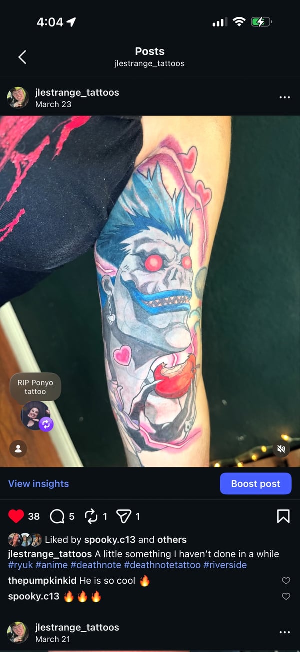 A colorful anime-style tattoo of Ryuk from Death Note on the forearm, featuring vibrant blues and reds with a heart motif — by Jessica Linden, riverside, ca