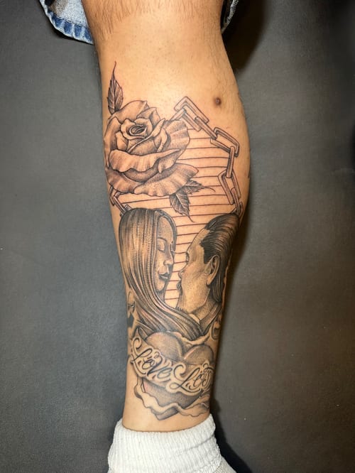 A black and grey realism tattoo on the calf depicting a couple's portrait with a rose and script reading 'Live Life' — by Humilde tattoos, los angeles