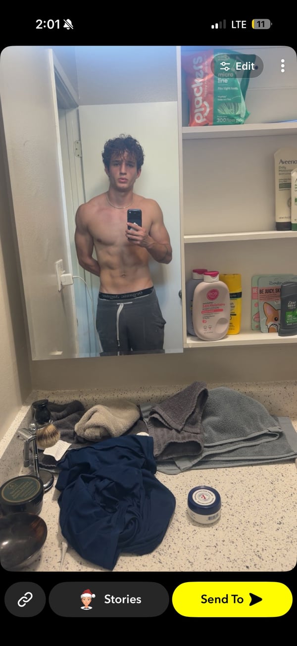 The image shows a person taking a mirror selfie in a bathroom, with no visible tattoos — by hii, los angeles