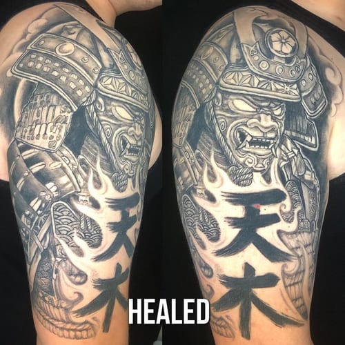 A bold black and grey tattoo of a samurai warrior in armor on the upper arm, featuring intricate details and script — by Sandra Price, los angeles