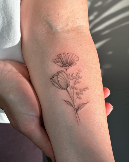 A delicate fine line black and grey flower bouquet tattoo on the forearm, featuring detailed floral elements — by Melanie Benoit, los angeles