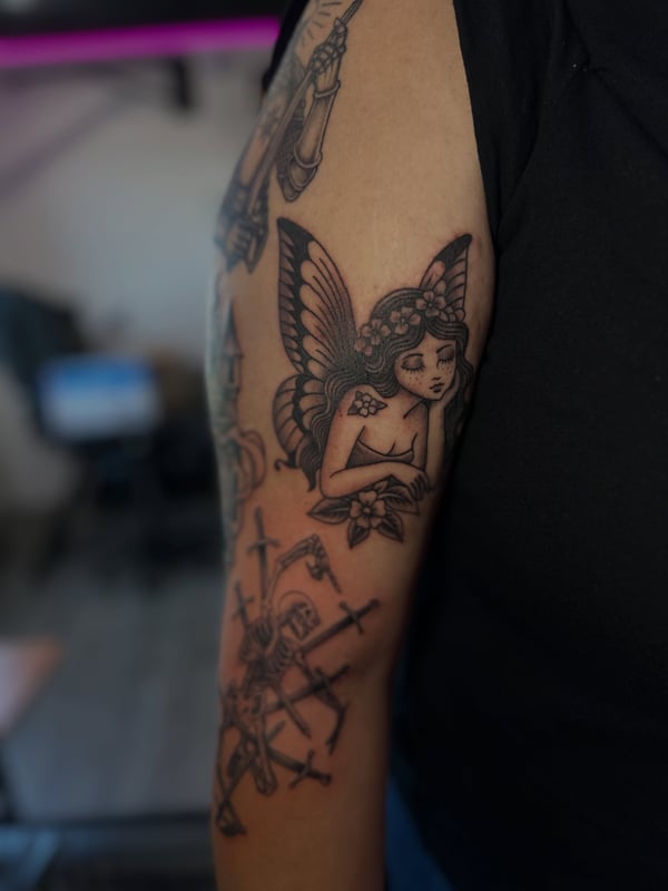 A traditional black and grey fairy with flowers on the upper arm — by Maddie Ramirez, palm desert, ca