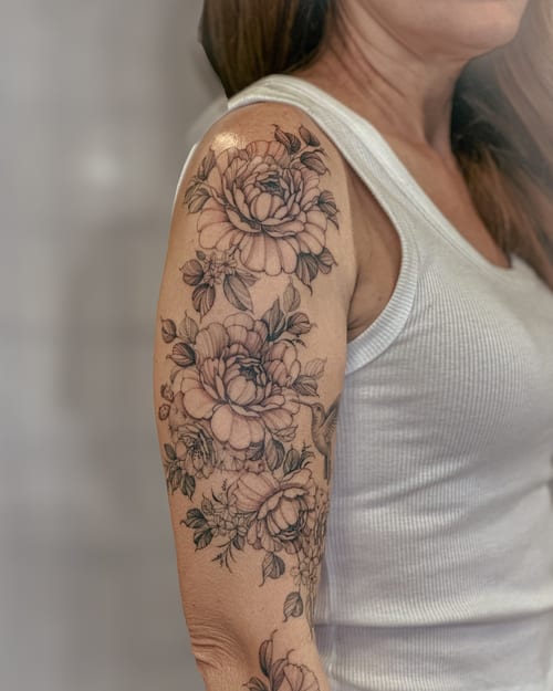 A delicate black and grey floral bouquet tattoo on the upper arm with intricate detailing and shading — by Melanie Benoit, los angeles