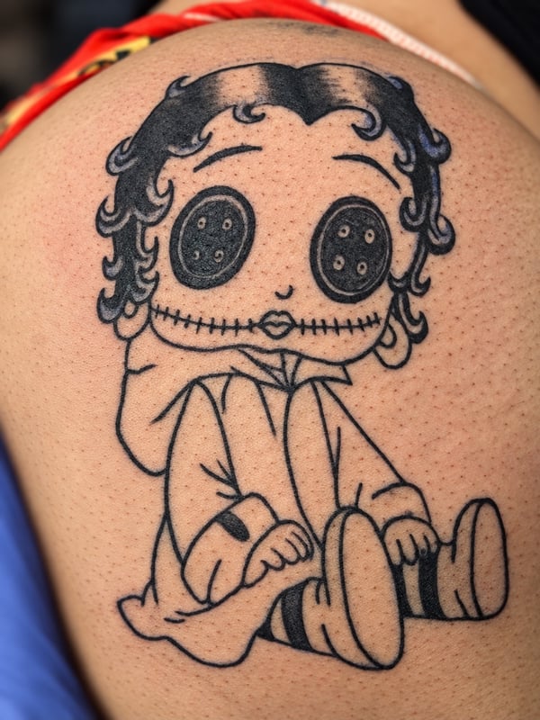 A whimsical blackwork tattoo of a doll with button eyes on the shoulder, featuring illustrative line art — by HEAVY INK, chino, ca