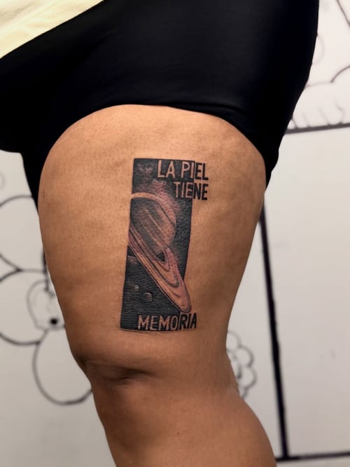 A black and grey tattoo of a planet with text on the thigh, featuring a graphic and illustrative style — by zealous, los angeles