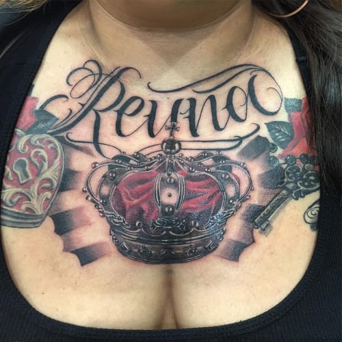 A bold Chicano style tattoo on the chest featuring a crown with colorful details and script lettering — by Johnny Ayala, los angeles
