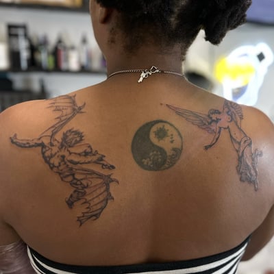A black and grey yin yang tattoo with an angel and demon on the back, featuring fine line and dark art style — by Maddie Ramirez, los angeles