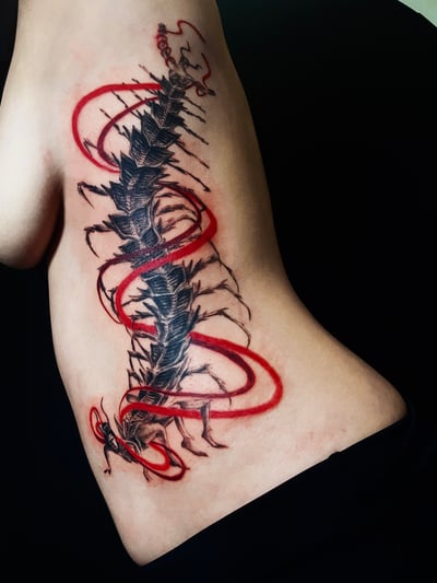 An abstract black and red dragon tattoo on the rib, featuring bold blackwork with red accents and dynamic lines — by zitronxus, los angeles