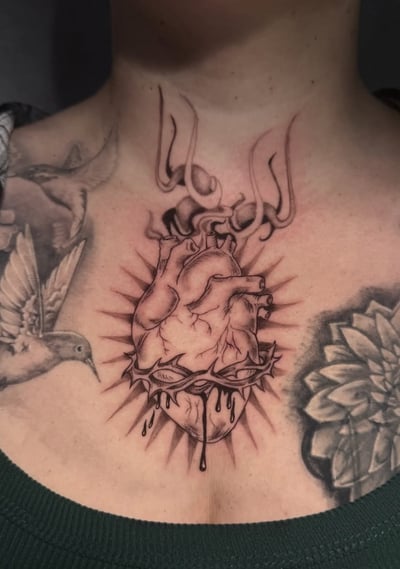 A black and grey illustrative tattoo of an anatomical heart with dripping details and rays on the chest — by Shelby Bianco, los angeles