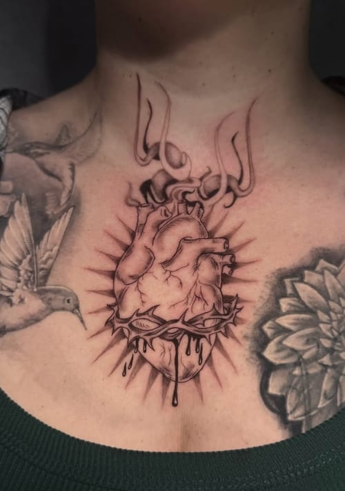 A black and grey illustrative tattoo of an anatomical heart with dripping details and rays on the chest — by Shelby Bianco, los angeles