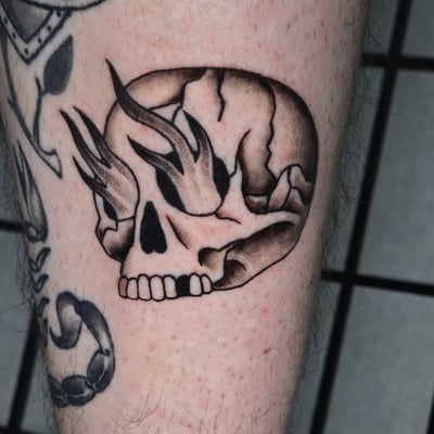 A bold black and grey flaming skull tattoo on the leg with strong graphic lines and shading — by Miguel ANGELO, los angeles