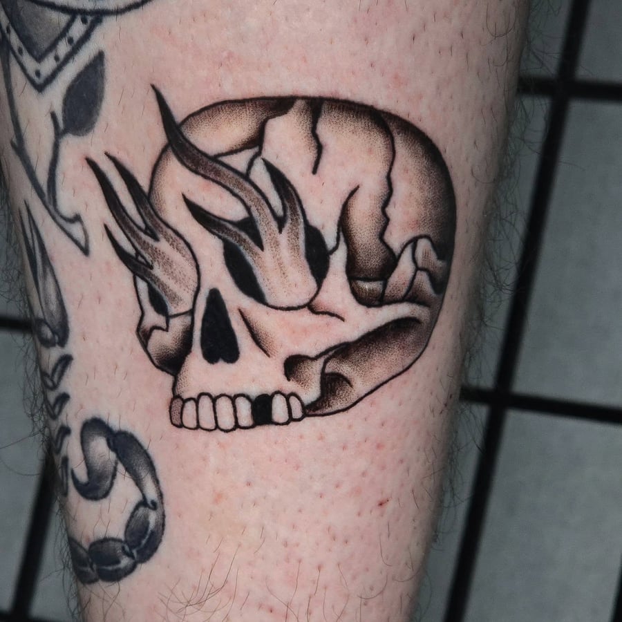 A bold black and grey flaming skull tattoo on the leg with strong graphic lines and shading — by Miguel ANGELO, los angeles