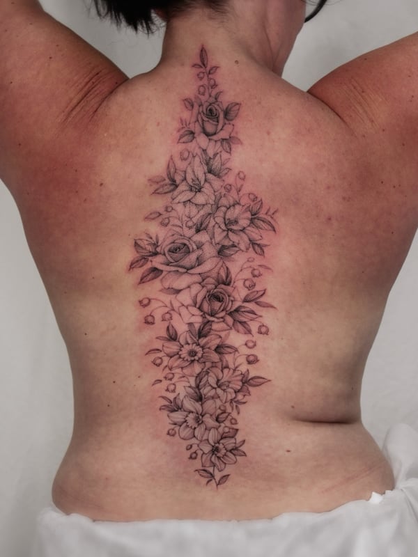 A delicate black and grey floral arrangement tattoo on the back featuring roses and other flowers — by Melanie Benoit, los angeles