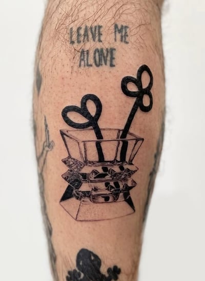 A blackwork tattoo on the leg featuring a stylized box with heart-shaped objects and the script 'LEAVE ME ALONE' above it — by Level tattoo, los angeles