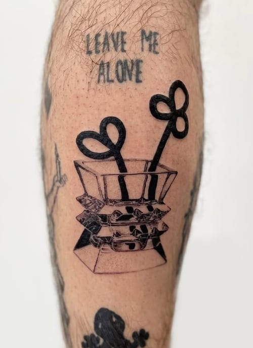 A blackwork tattoo on the leg featuring a stylized box with heart-shaped objects and the script 'LEAVE ME ALONE' above it — by Level tattoo, los angeles
