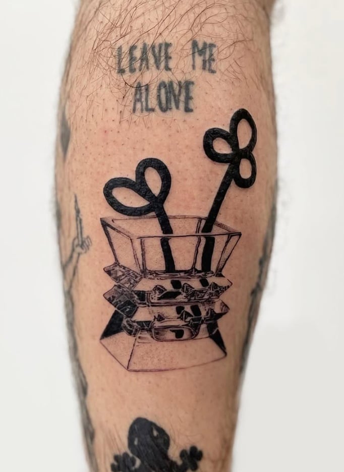 A blackwork tattoo on the leg featuring a stylized box with heart-shaped objects and the script 'LEAVE ME ALONE' above it — by Level tattoo, los angeles