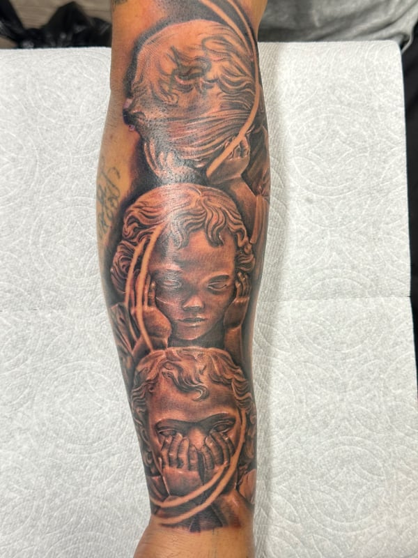 A detailed black and grey realism tattoo on the forearm depicting multiple angelic faces with intricate shading — by Humilde tattoos, los angeles