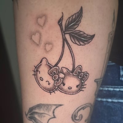 A whimsical black and grey tattoo of cherries with cat faces on the arm, featuring delicate heart accents — by Miguel ANGELO, los angeles