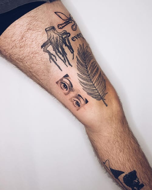 A black and grey tattoo featuring an eye and a feather on the thigh, done in a graphic blackwork style — by Level tattoo, los angeles