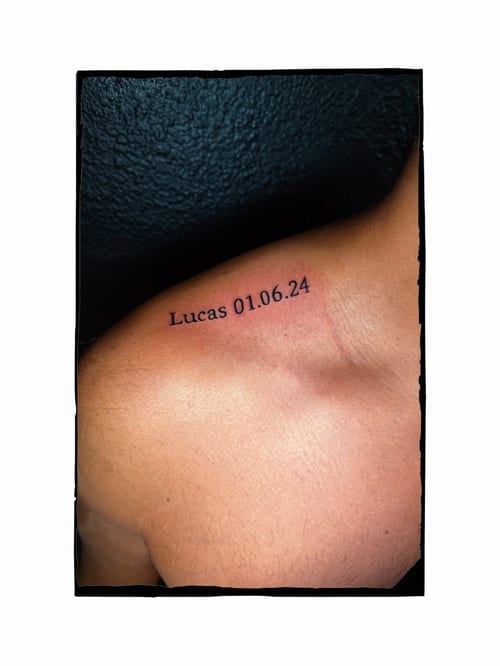A minimalist black and grey tattoo featuring a name and date on the shoulder — by Kiera Garvin, los angeles