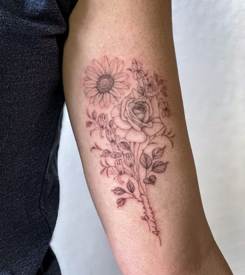A delicate black and grey floral bouquet tattoo on the inner arm, featuring roses and other flowers in fine line style — by Melanie Benoit, los angeles